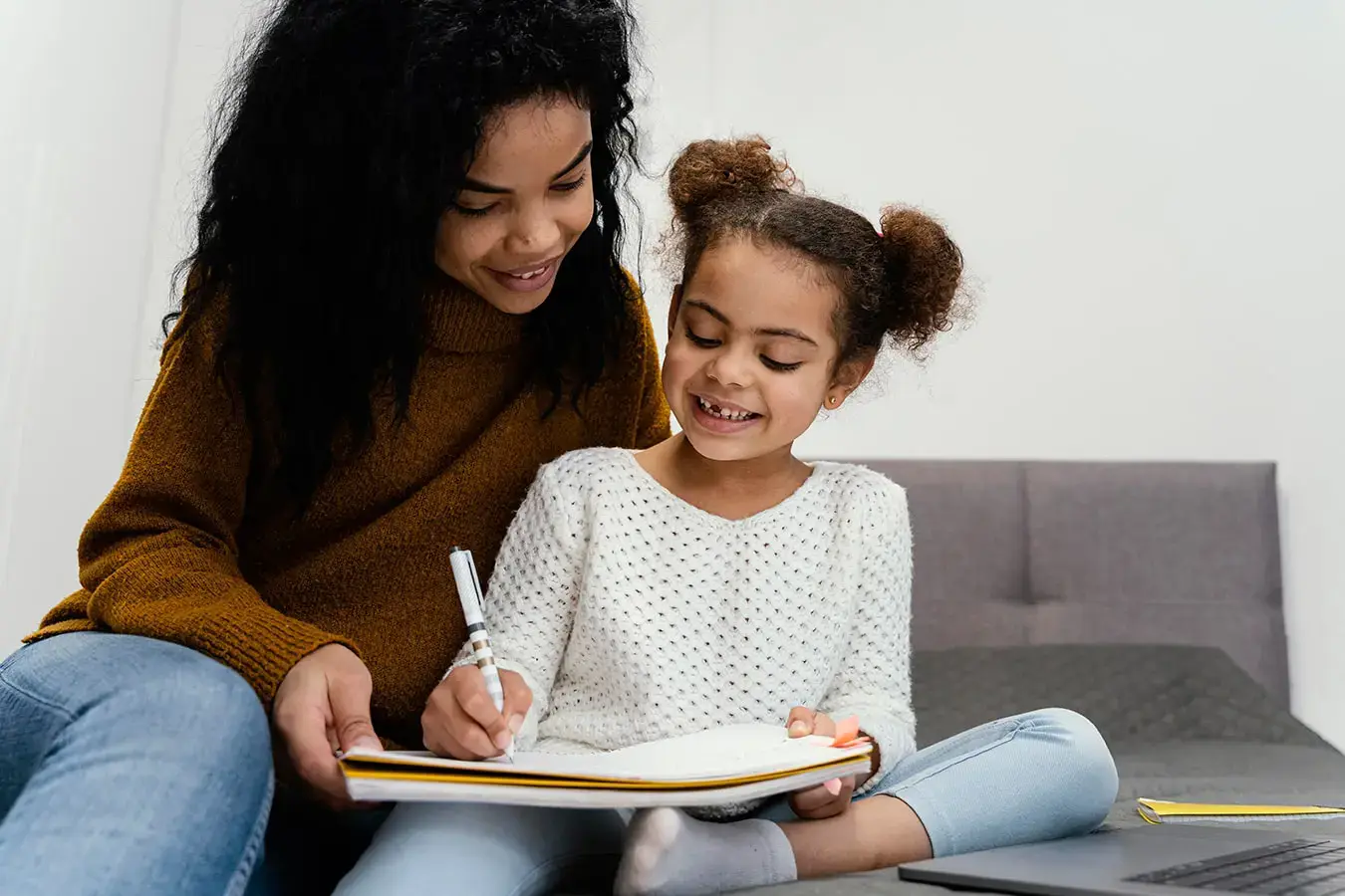 Smiling child writing in a notebook with mom