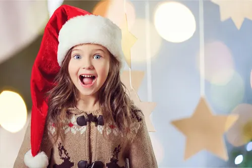 smiling girl wearing a santa hat and a christmas sweater with hanging stars in the background