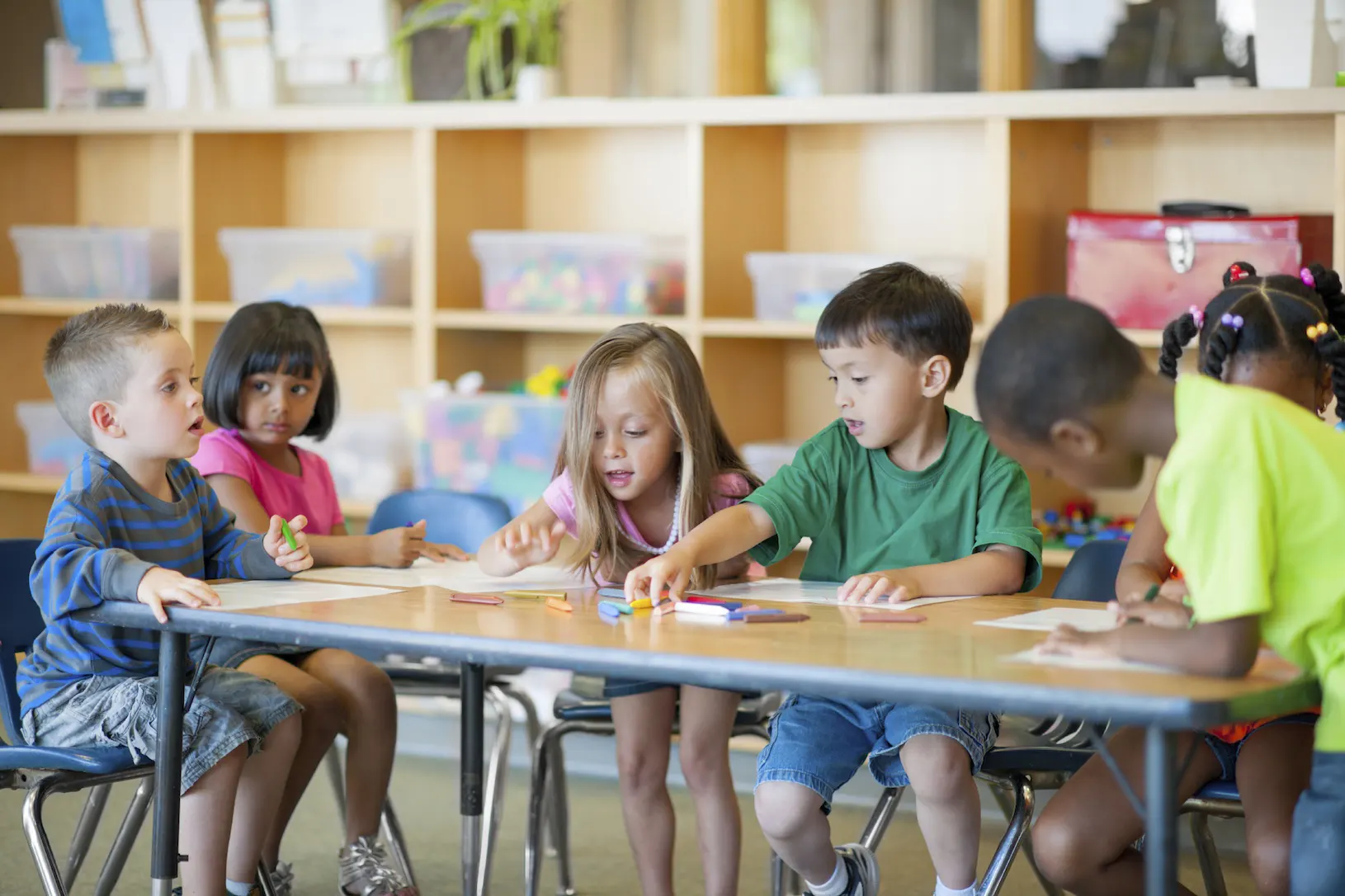 kids sitting around classroom table with paper and crayons